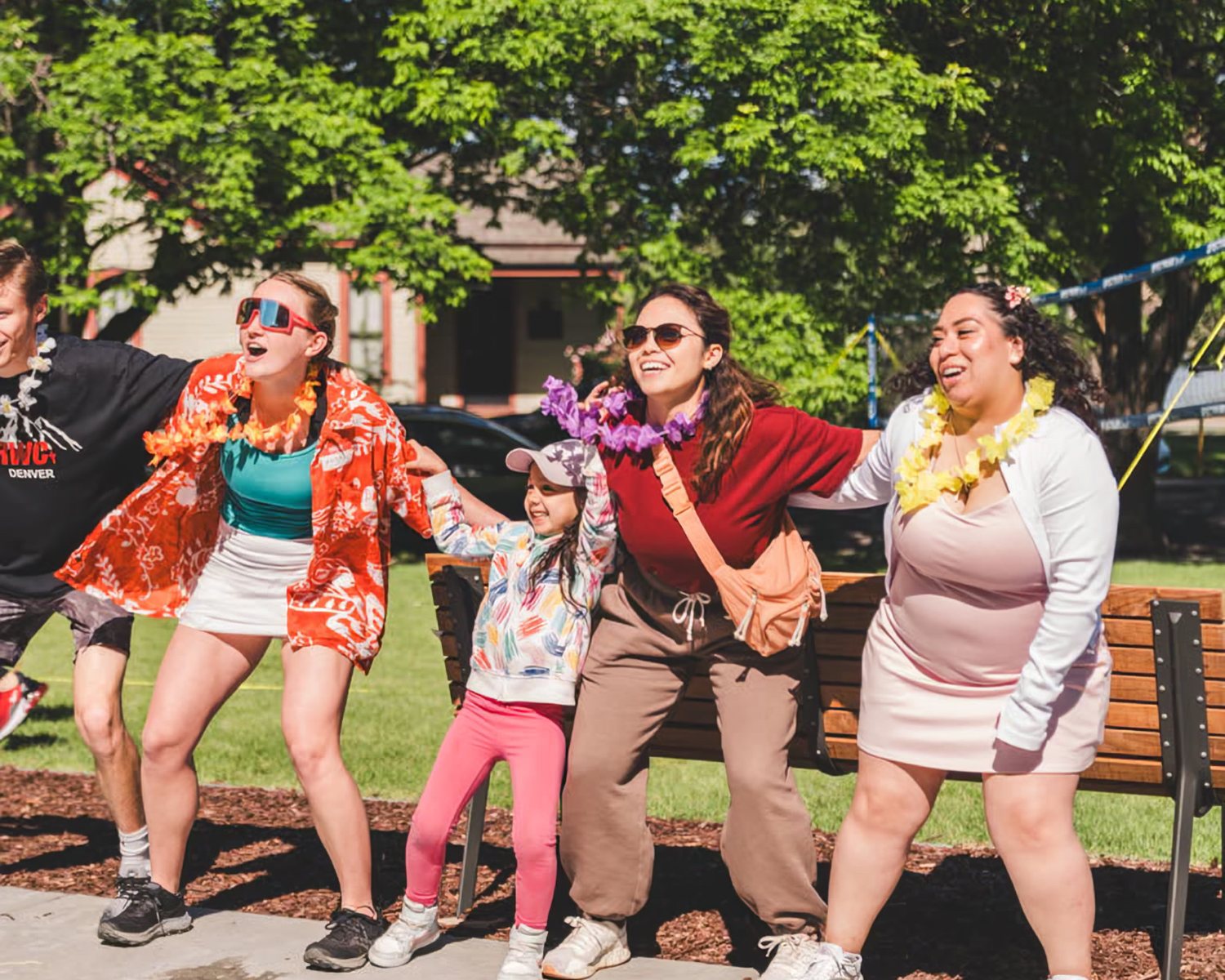 Families in leis laughing together on a bench at an RWC Denver event