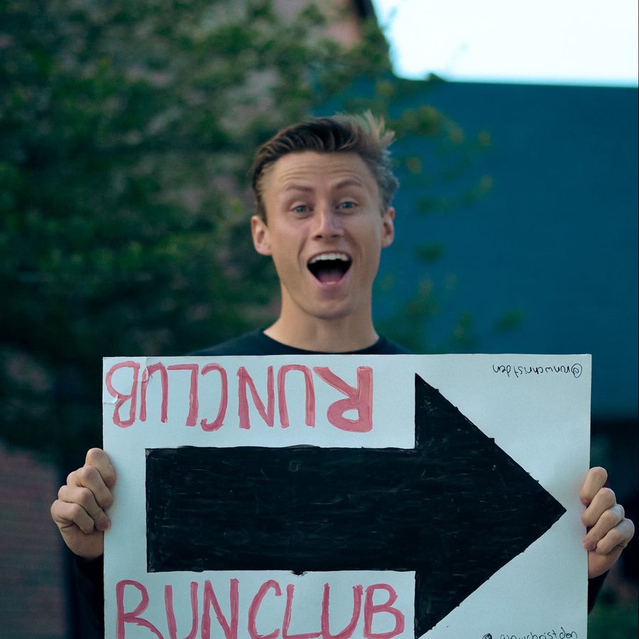 A volunteer holding a hand-drawn Run Club arrow sign