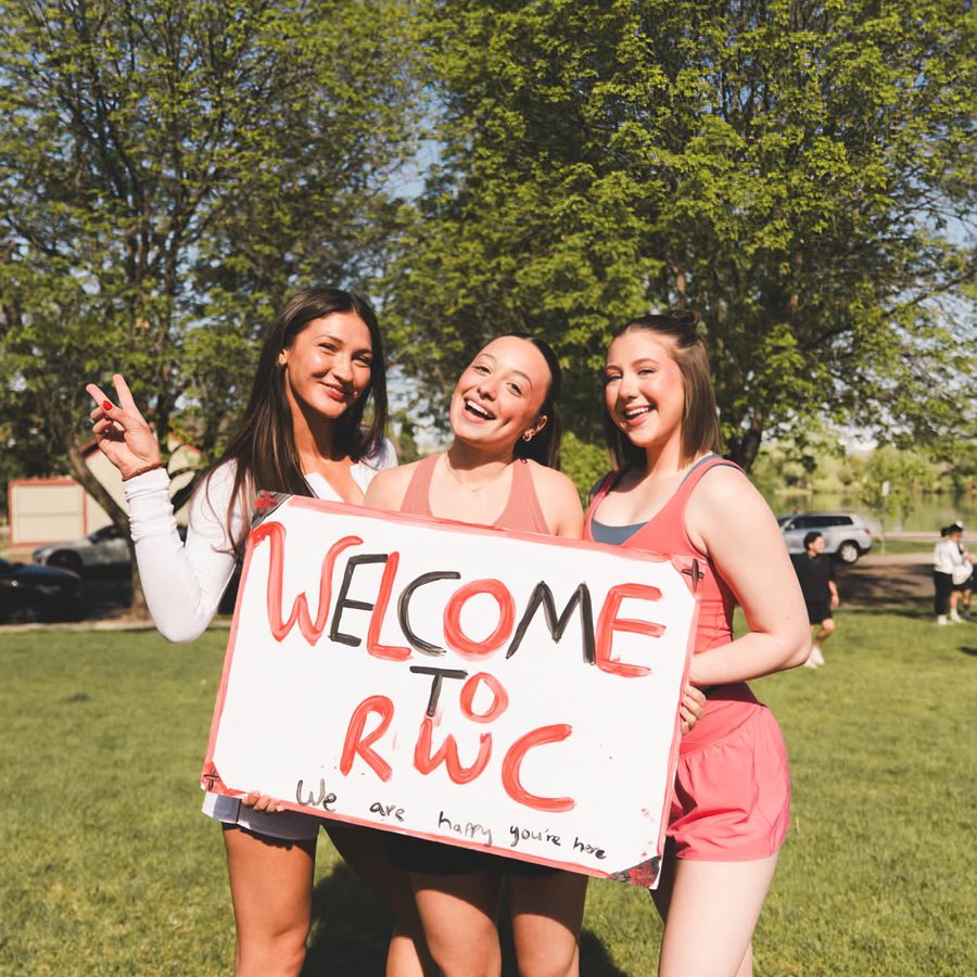Three women holding up a hand-painted Welcome to RWC sign